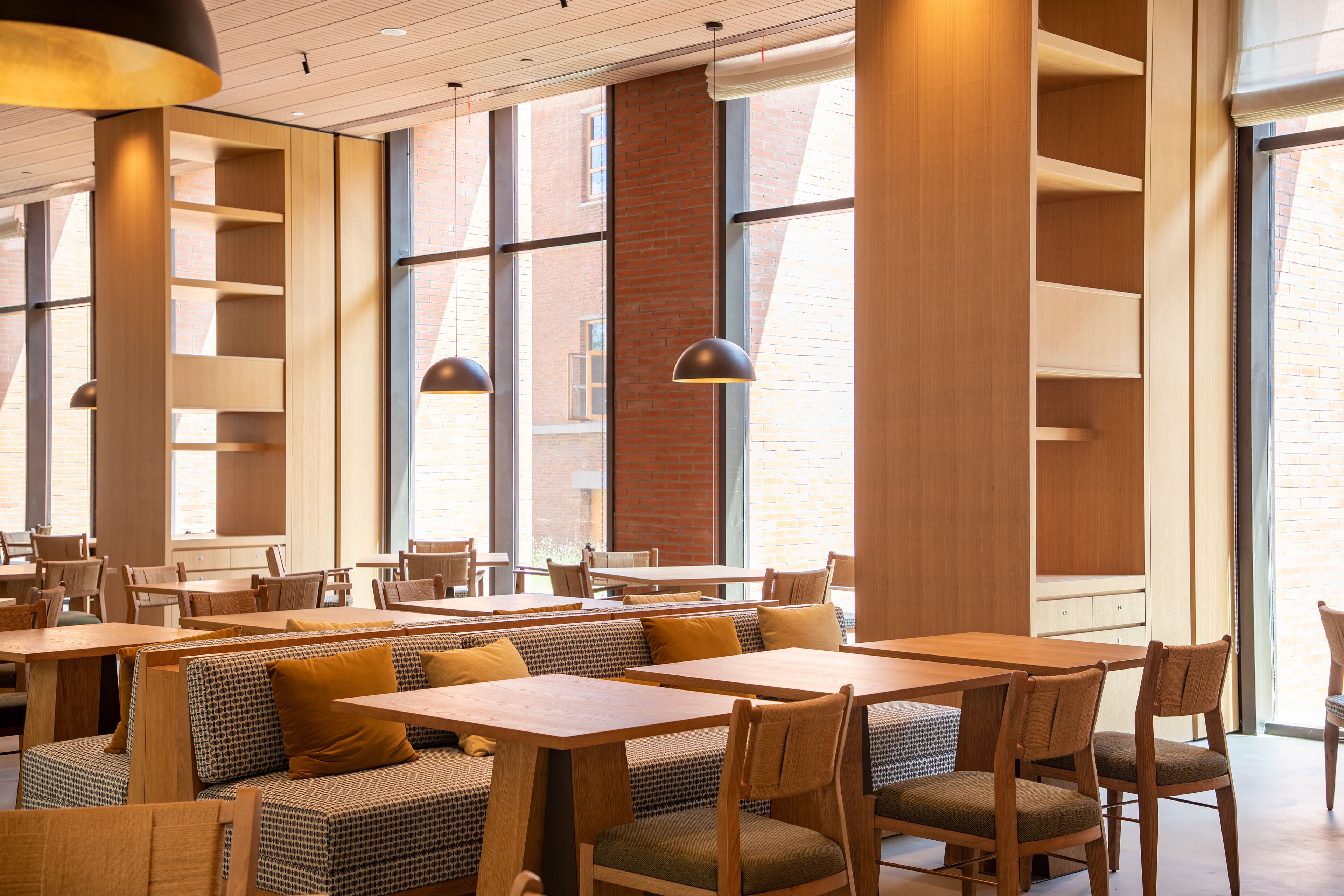 A modern restaurant interior with high ceilings, large windows, and a mix of seating options including booths and tables.