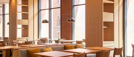 A modern restaurant interior with high ceilings, large windows, and a mix of seating options including booths and tables.