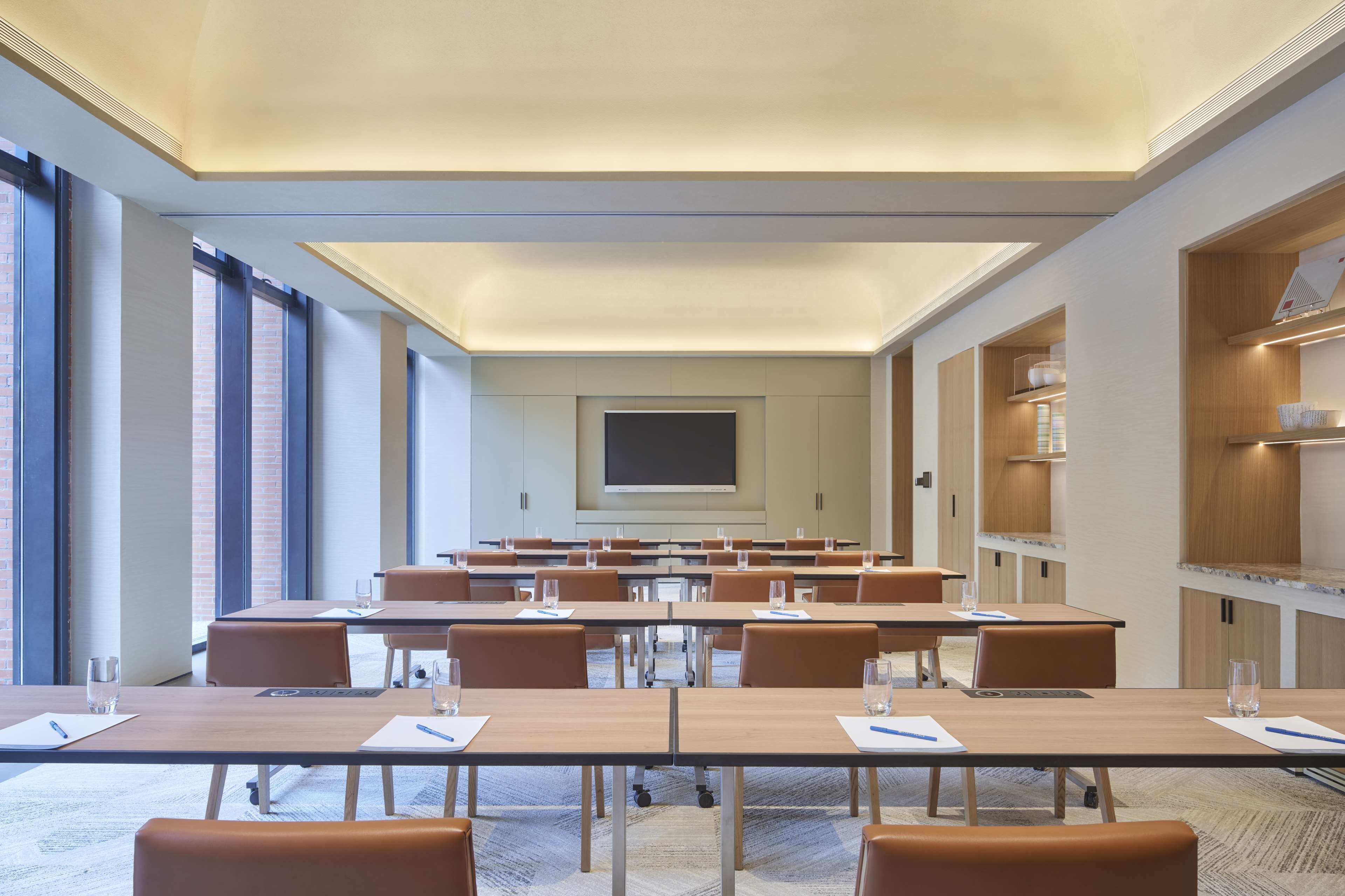 Une salle de conférence équipée de longues tables, de chaises, d’un grand écran et d’étagères intégrées.
