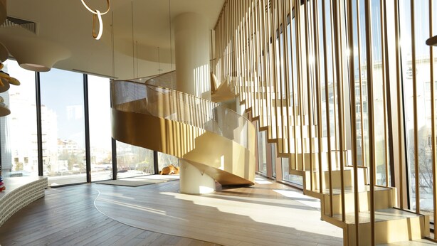 Un interior moderno con una escalera curva, ventanas amplias y suelo de madera.