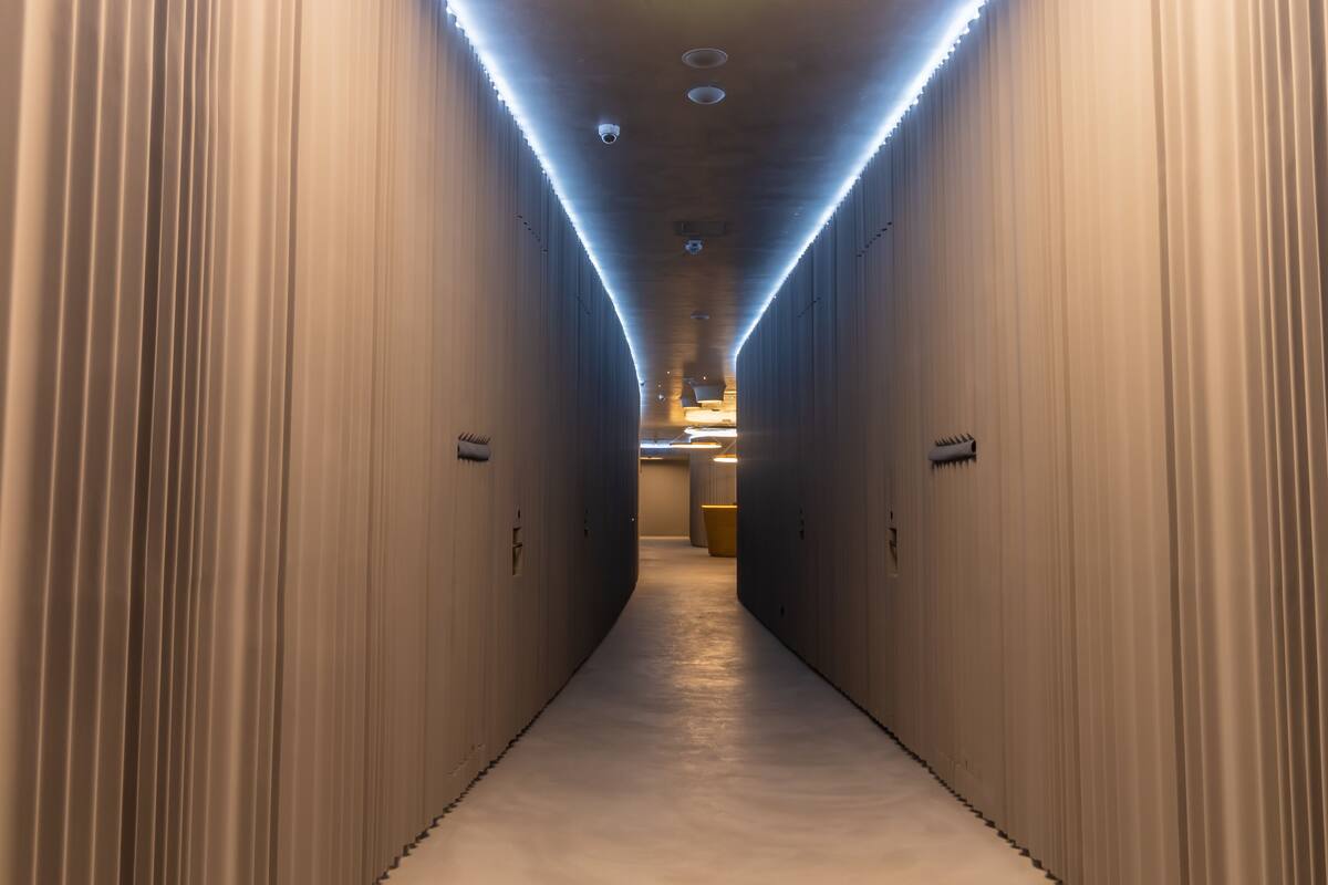 A corridor with a smooth, reflective floor and walls, leading to a bright area at the end.