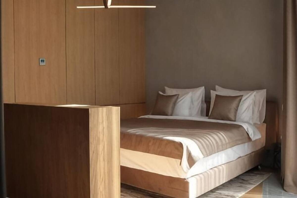 A bedroom with a bed, wooden wardrobe, and a ceiling light fixture.