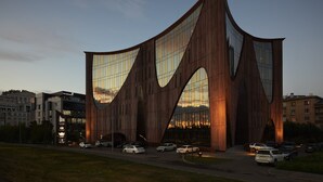 Un edificio moderno con un diseño curvo único y ventanas amplias que reflejan el atardecer.