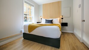 A modern bedroom with a large bed, a window, a bedside table with a lamp, and a wall-mounted TV. - Bright Loft · Queen Bed | Walk Everywhere (Québec City)