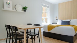 A modern bedroom with a bed, bedside table, lamp, and a window with a view of the street. - Bright Loft · Queen Bed | Walk Everywhere (Québec City)