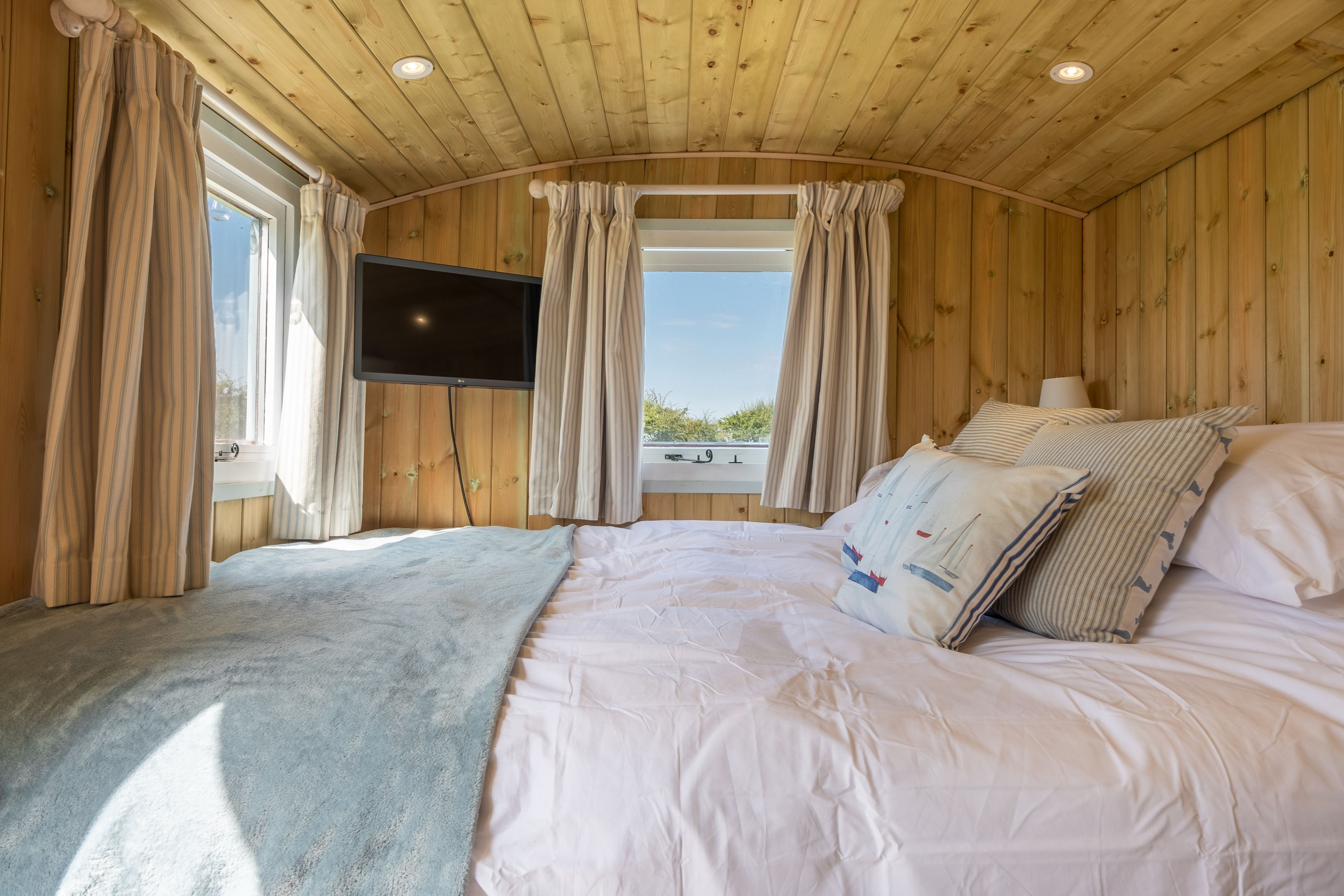 Ein Zimmer mit Holzwänden, einem Bett, Vorhängen, einem Flachbildfernseher und einem Fenster mit Aussicht.
