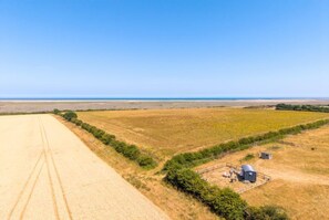 A vast agricultural field with a clear sky, a dirt road, and a small structure with a fenced area. - Dog-friendly glamping hut in the North Norfolk Coast (Stiffkey)
