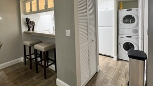 A compact kitchen with a built-in oven, a washing machine, and a small bar area with stools. - Beautiful Cottage located inside PGA National (Palm Beach Gardens)