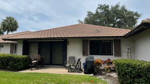 A two-story house with a tiled roof, a covered patio with outdoor furniture, and a small garden area. - Beautiful Cottage located inside PGA National (Palm Beach Gardens)