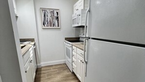 A narrow kitchen with white cabinets, a microwave, and a refrigerator. - Beautiful Cottage located inside PGA National (Palm Beach Gardens)