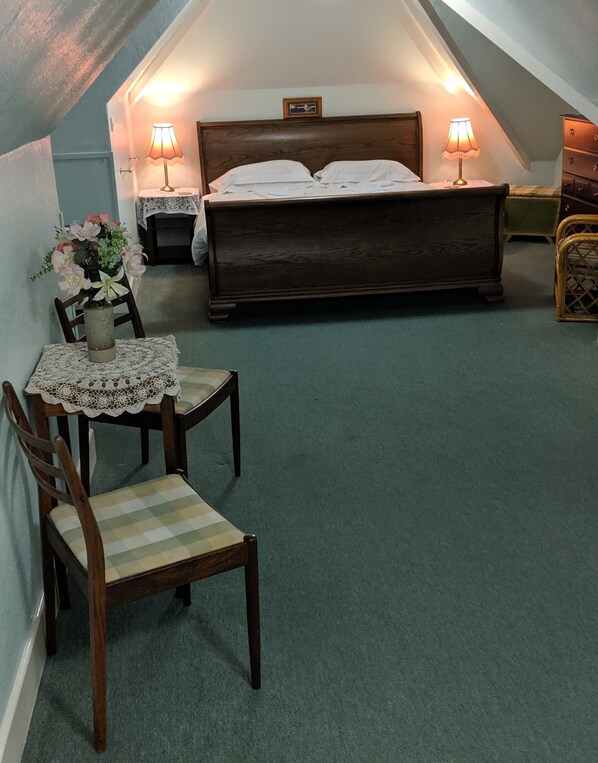 A cozy attic bedroom with a large bed, two bedside lamps, a wooden chair, and a small table with a vase of flowers. - Huntingball Lodge (Minehead)
