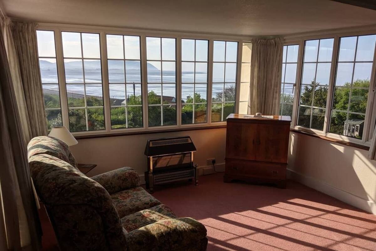 A room with large windows, a sofa, a wooden cabinet, and a radiator.