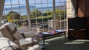A cozy living room with a large window offering a scenic view of the sea and hills.