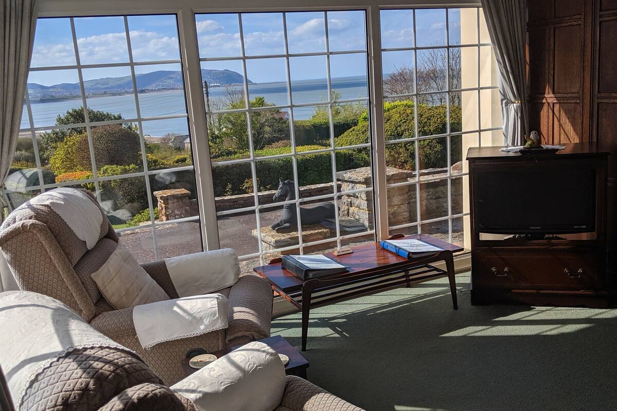 A cozy living room with a large window offering a scenic view of the sea and hills.
