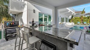 Une cuisine extérieure moderne dotée d’un bar, d’une piscine et d’un patio avec des chaises longues.