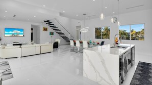 Une cuisine moderne avec un îlot en marbre, un coin repas avec des chaises blanches et un escalier menant à un autre niveau.