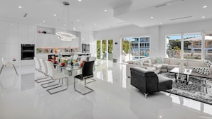 Un vaste espace de vie comprenant une cuisine moderne, une table à manger avec des chaises, un canapé gris et un tapis à motifs.