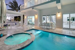 A modern indoor pool area with a hot tub, seating, and a view of the outside. - 4BR/5BA Waterfront, Pool & Hot Tub, Deep Canal, Bikes, Near Beach, near Gulf/Atl (Marathon)