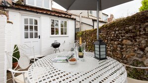 Un espace extérieur aménagé pour les repas, avec une table ronde, des chaises, une bouteille de champagne et une lanterne.