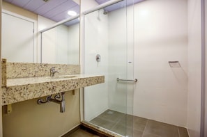 Un baño con lavamanos de encimera de granito, cabina de ducha de vidrio y suelo de baldosas blancas.