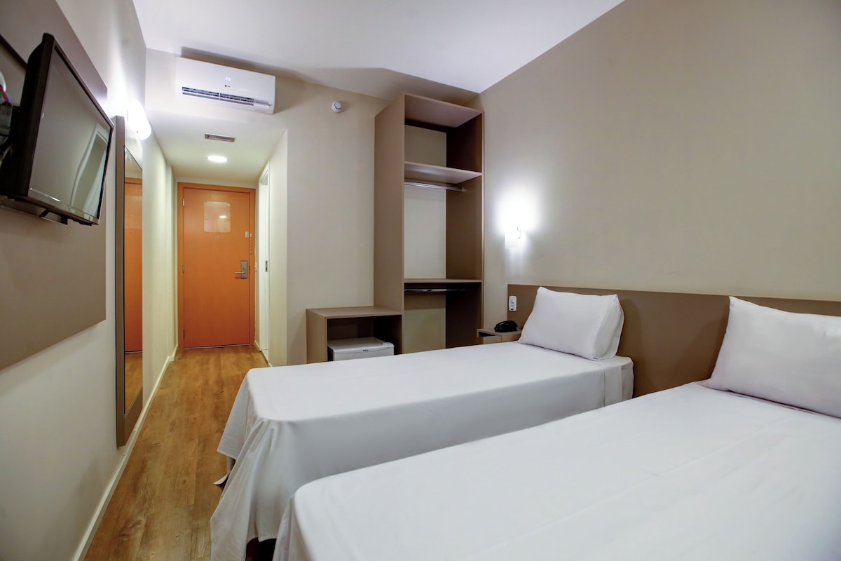 Habitación de hotel con dos camas, televisión, armario y escritorio.