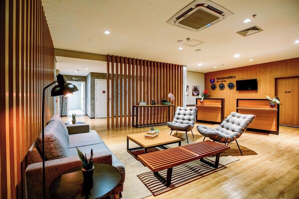 A modern hotel lobby with a sofa, armchairs, a coffee table, and a reception desk.