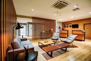 Un moderno vestíbulo de hotel con un mostrador de recepción de madera, un sofá, dos sillones, una mesita de café y una lámpara.