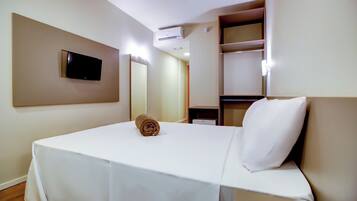 Een hotelkamer met een bed, een aan de muur bevestigde televisie, een spiegel en een plank met enkele spullen.