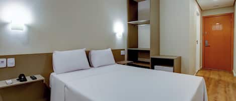 A hotel room with a bed, bedside tables, a desk, a wardrobe, and a door.