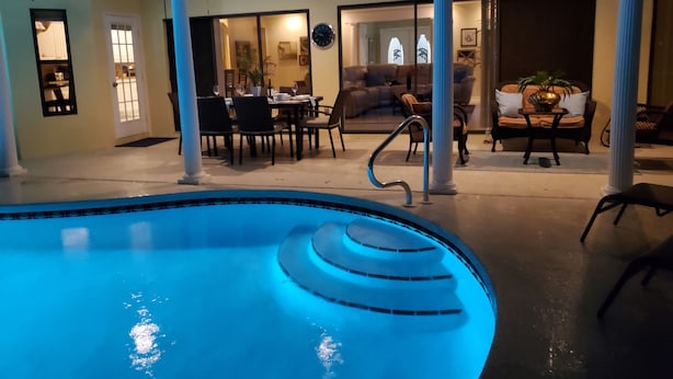 Une piscine au design original, un espace repas avec des tables et des chaises, et un salon avec un canapé et une table basse.