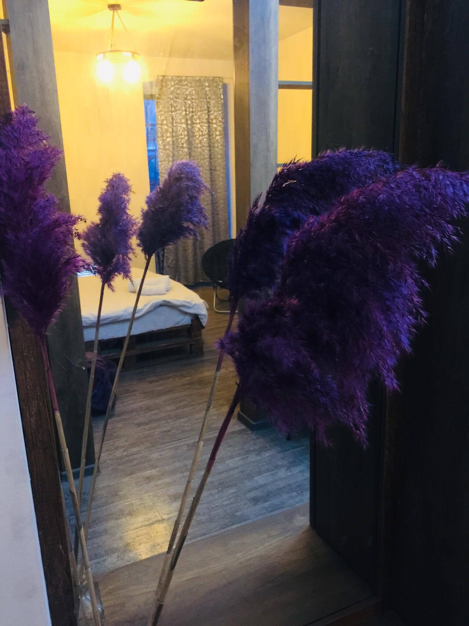 Et værelse med en seng, en stol og høje lilla planter foran.
