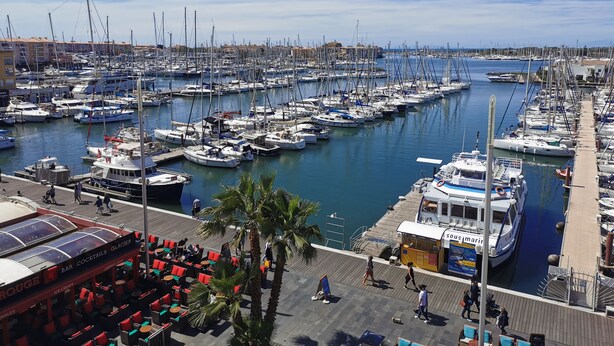 Een jachthaven met talloze boten afgemeerd, een bar met terras en uitzicht op het water.