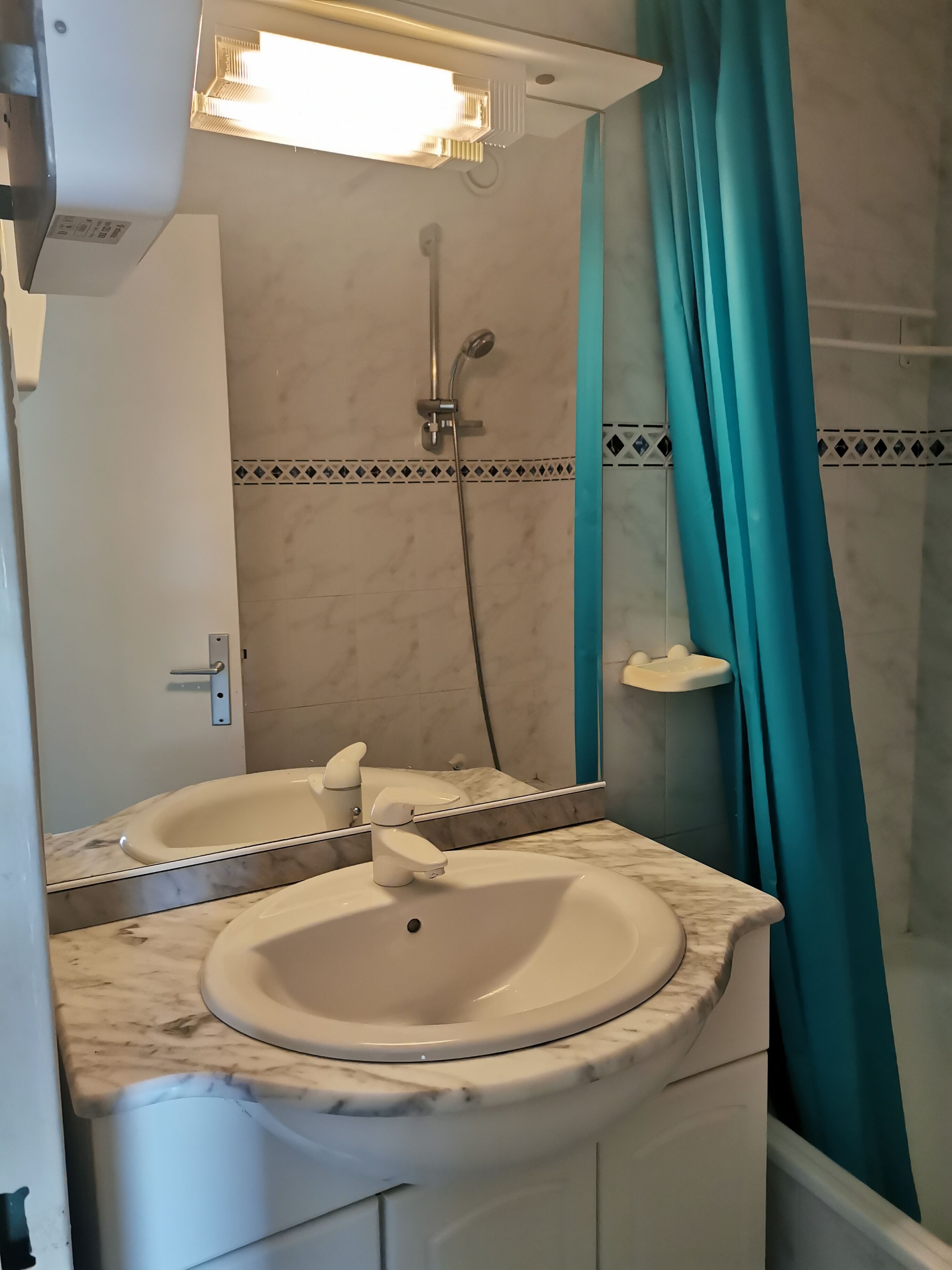 A bathroom with a white sink, a mirror, a shower, and a teal shower curtain.