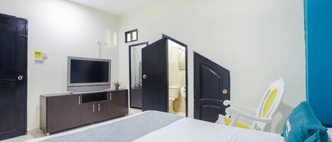 Un dormitorio con cama, televisión, armario y baño visible a través de una puerta abierta.