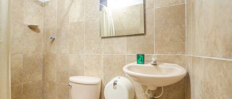 Un baño con azulejos color beige, un inodoro, un lavabo, un cabezal de ducha de mano y un espejo.