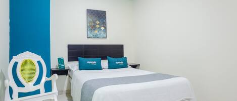 Una habitación de hotel con una cama, una mesita de noche, una silla y una obra de arte en la pared.