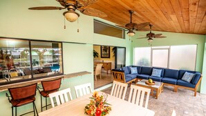 A spacious living area with a dining table, white chairs, a blue sofa, and two ceiling fans. - Palm Tree III Pool Home Waterfront  (Apollo Beach)