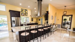 A modern kitchen with a central island, bar stools, and a large island with a stainless steel refrigerator. - Palm Tree III Pool Home Waterfront  (Apollo Beach)