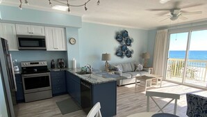 A modern kitchen with a central island, a dining area with a table and chairs, and a living area with a sofa and decorative wall art.