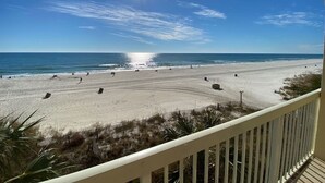A beach view from a balcony with a railing, sandy beach, and ocean.