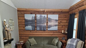A cozy living room with a wooden wall, a fireplace, a green sofa, a wooden coffee table, and a large landscape painting. - Log Cabin 2 at Osborn Boat Ramp on Patoka Lake (Jackson Township)