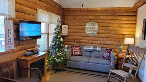 A cozy cabin interior with a wooden log wall, a television, a Christmas tree, a sofa, and a rocking chair. - Log Cabin 4 at Osborn Boat Ramp on Patoka Lake (Jackson Township)