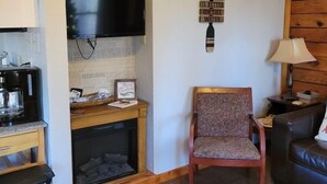 Un salon chaleureux avec une cheminée, un téléviseur fixé au-dessus, un mur en bois orné d’une décoration, un fauteuil confortable et un canapé.