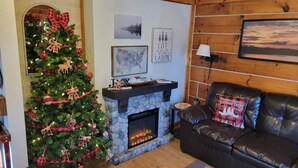 A cozy living room with a fireplace, a Christmas tree, and a leather couch. - Log Cabin 7 with Hot Tub at Osborn Boat Ramp at Patoka Lake (Jackson Township)