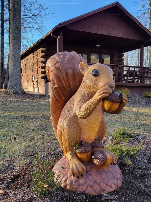 A large wooden sculpture of a squirrel holding an acorn, placed on a circular base with a log.