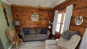 A cozy cabin-style room with a wooden ceiling, a sofa, a patterned armchair, a wooden chair, and a rug. - Log Cabin 9 at Osborn Boat Ramp on Patoka Lake (Jackson Township)