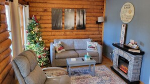 L’intérieur chaleureux d’un chalet en bois avec une cheminée, un sapin de Noël, un canapé agrémenté de coussins décoratifs et une table basse.