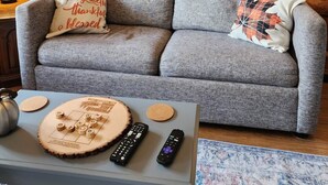 Un salon chaleureux avec un canapé gris, une table basse sur laquelle est posé un jeu de société et trois télécommandes.