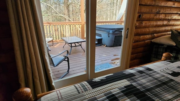Une chambre dotée d’un grand lit, d’une porte-fenêtre coulissante donnant sur une terrasse extérieure et d’un intérieur de style cabane en bois.