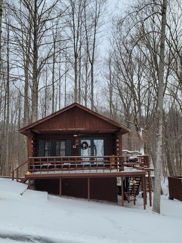 Une cabane en bois dotée d’un balcon, entourée d’arbres et recouverte de neige.